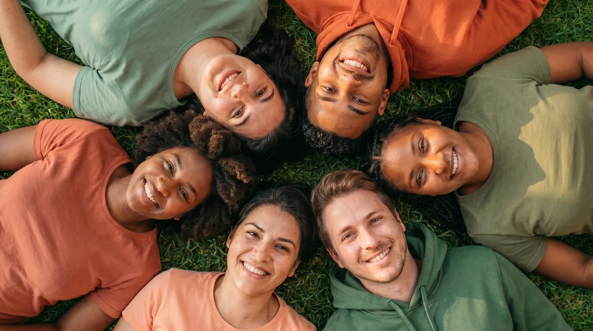 Grupo de personas recostadas en círculo sobre el pasto, sonriendo